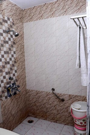 Un baño con pared de baldosas a cuadros, una ducha, un asidero y un inodoro con un balde rosa y blanco.
