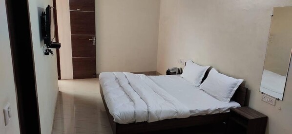 Cama bem arrumada com roupa de cama branca em quarto com porta de madeira e pequena mesa de cabeceira.