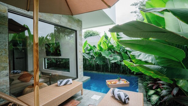 A modern outdoor lounge area with a pool, wicker furniture, and lush tropical plants. - The Reef Villas (Pecatu)