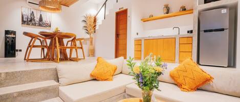 A modern kitchen with a built-in microwave and refrigerator, a dining area with a wooden table and chairs, and a living area with a sofa and decorative pillows.