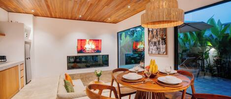 A modern kitchen with wooden cabinetry, a dining area with a round table and chairs, and a large window overlooking a garden.