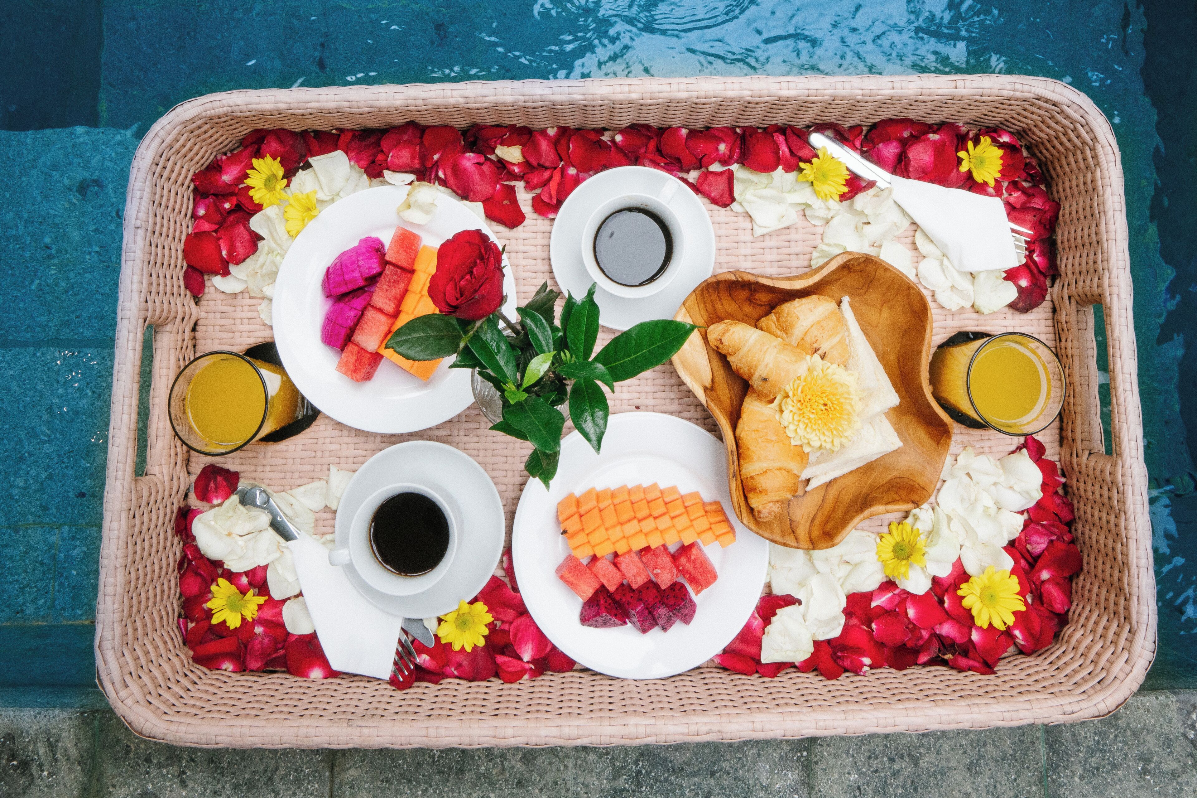 Bandeja de desayuno con frutas, pasteles y bebidas sobre una mesa junto a la piscina.