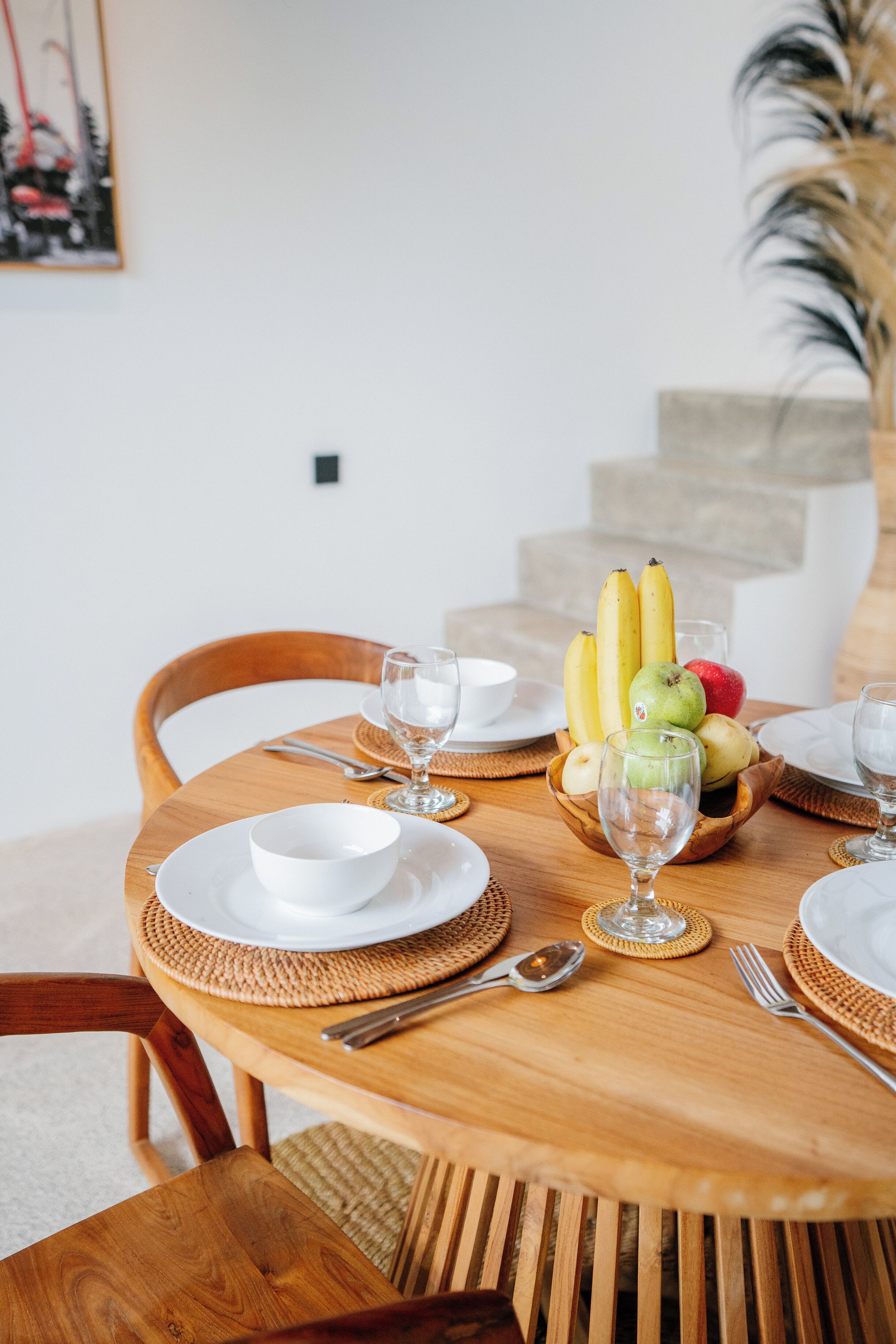 A wooden dining table set with plates, bowls, cutlery, and a fruit bowl.