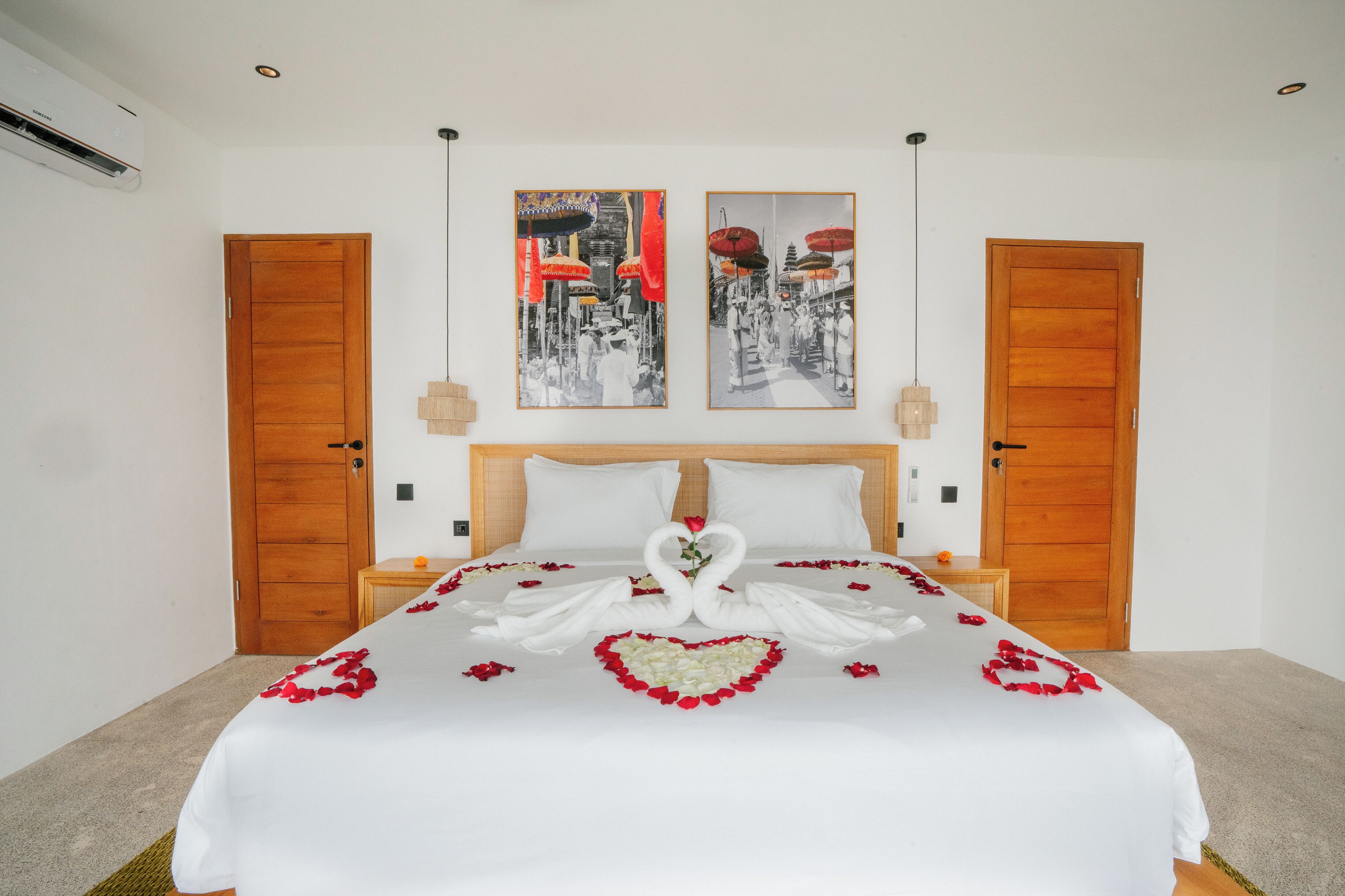 Una cama impecablemente hecha con un arreglo de pétalos de rosa en forma de corazón y dos almohadas con forma de cisne.