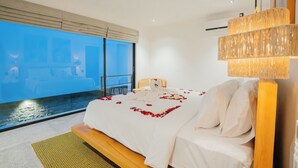 A modern hotel room with a large bed, a view of the sea, and a unique chandelier. - The Reef Villas (Pecatu)