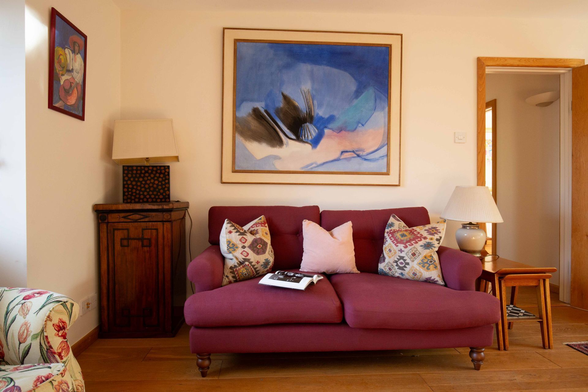 A living room with a red sofa, patterned cushions, a wooden cabinet, and a painting on the wall.