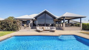 A modern house with a swimming pool, outdoor seating, and a covered patio.