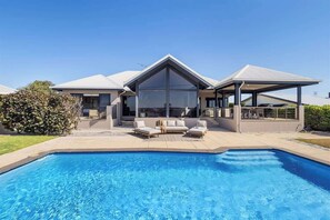 A modern house with a swimming pool, outdoor seating, and a covered patio.
