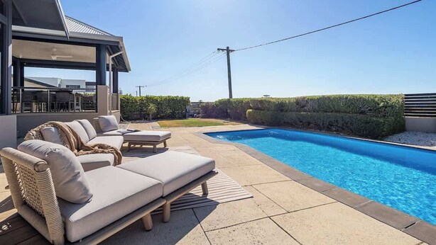 Un área de piscina moderna al aire libre con una silla de descanso y un espacio de estar techado.