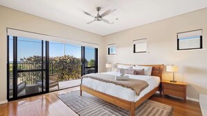 A bedroom with a large bed, a ceiling fan, a view through a sliding glass door, and a nightstand with a lamp.