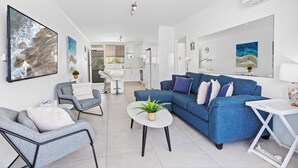 A modern living room with a blue sofa, grey armchairs, and a white coffee table with a plant. - Palm Beach Waterfront Escape (Palm Beach)