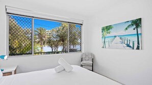 A hotel room with a bed, a chair, a desk, and a large window with a view of palm trees and a beach. - Palm Beach Waterfront Escape (Palm Beach)