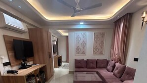 A modern living room with a sectional sofa, a TV, and a ceiling fan. - AATITHYAM RESIDENCY (Gurugram)