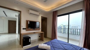A hotel room with a bed, a TV, a desk, and a view of the city. - AATITHYAM RESIDENCY (Gurugram)