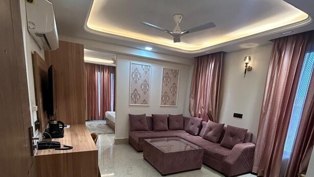A modern living room with a sectional sofa, a coffee table, and a wooden desk with a flat-screen TV. - AATITHYAM RESIDENCY (Gurugram)