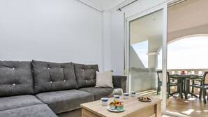 A modern living room with a grey sectional sofa, a wooden coffee table with decorative items, and a sliding glass door leading to an outdoor dining area.