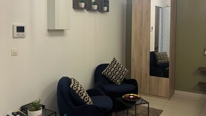 A modern living room with two dark blue sofas, a small side table with a plant, and a coffee table. There are three hanging pendant lights, a wall-mounted air conditioner, and a mirror reflecting the room. - Lovely studio, ideal for a couple!  (Schoelcher)