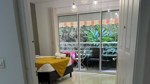 A hotel room with a bed, a small table with a plant, and a balcony with a table and chairs. - Lovely studio, ideal for a couple!  (Schoelcher)