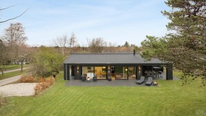Una casa moderna con un amplio ventanal, una terraza con mobiliario exterior y un césped bien cuidado.