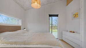 Un dormitorio con una cama grande, una ventana, una puerta que da al exterior y un estante en la pared con objetos.