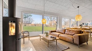 Una sala de estar moderna con chimenea, sofá de cuero y grandes ventanales con vistas a un jardín.