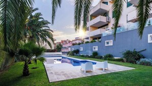 Un quartier résidentiel moderne doté d’une piscine, de chaises longues blanches et de palmiers.