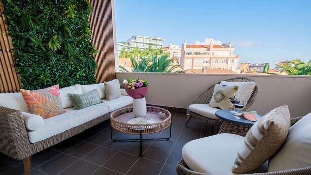 Un balcon avec un canapé en osier, une table basse ronde et des chaises en osier.