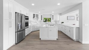 A modern kitchen with white cabinetry, stainless steel appliances, and a central island. - Glam Manor | 7,000 Ft Mansion with Waterslide | Sauna | Cold plunge (Sunrise)