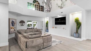 A spacious living room with a large sectional sofa, a mounted TV, and a staircase leading to an upper level. - Glam Manor | 7,000 Ft Mansion with Waterslide | Sauna | Cold plunge (Sunrise)