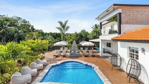 Área de piscina com espreguiçadeiras, guarda-sóis e uma piscina azul cristalina.