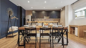 A modern kitchen with dark cabinets, a wooden dining table, and chairs. There is a hanging rack with folded towels and a mirror on the wall. - Suite 332 Brady – Stunning Duplex in Paris 10 (Paris)