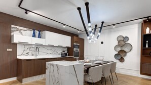 Een moderne keuken met marmeren aanrechtbladen, een centraal eiland en een eethoek met stoelen en een tafel.