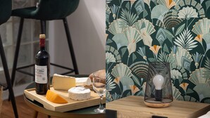 Een tafel met wijn, kaas en een glas, voor een achtergrond met bloemenbehang.