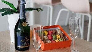 Una bottiglia di champagne Aguila, un bicchiere e una scatola di macarons su un tavolo con un'orchidea bianca.