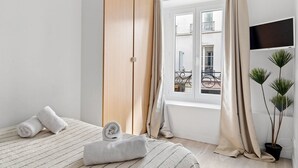Una camera da letto con un letto, un armadio in legno, una finestra con tende, una pianta in vaso e un televisore appeso al muro.