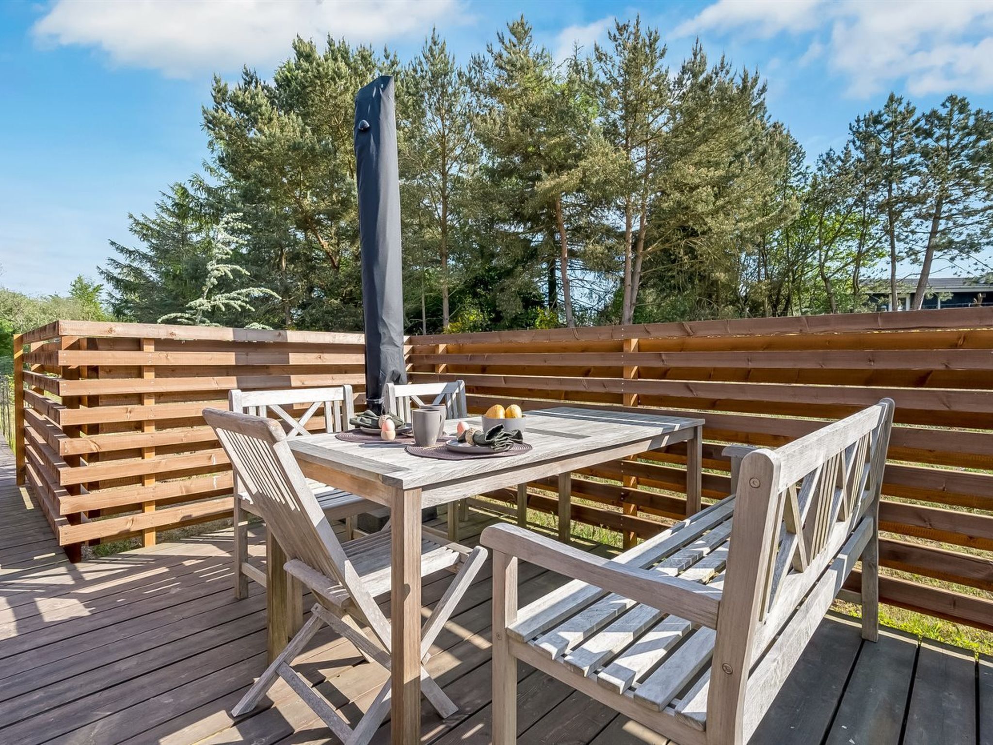 Una terraza de madera con mesa y sillas, una parrilla y una valla de madera.