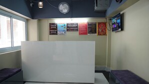 A reception area with a marble-tiled floor, a white reception desk, and purple cushioned seating. There are several informational posters on the wall, including one about Aashta Heights. - Hotel Aastha Height (Rishikesh)