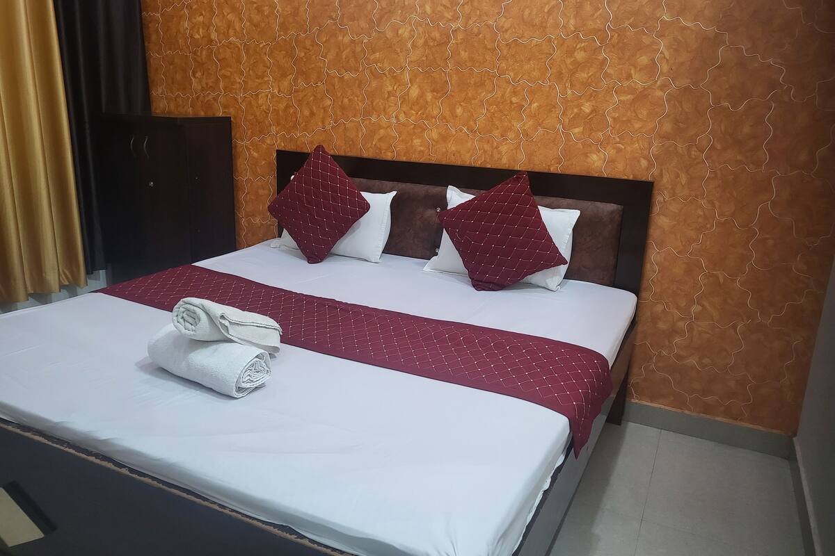 A neatly made bed with a white and maroon bedspread, two white pillows, and two maroon pillows. There is a rolled white towel on the bed.
