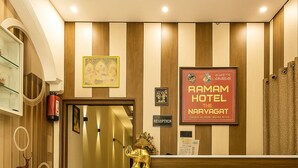 A reception area with a reception desk, a reception sign, a framed picture, a coat rack with a deer figurine, and a door leading to the rooms. - Ramam By Naavagat 700 Meter From Temple (Faizabad)