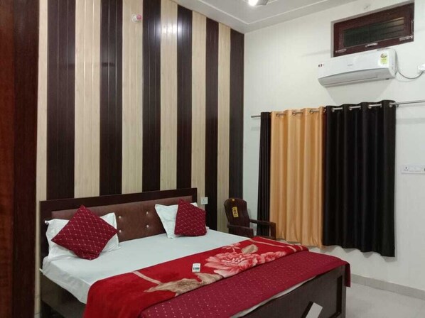 Un dormitorio con cama, una silla, aire acondicionado instalado en la pared y cortinas.