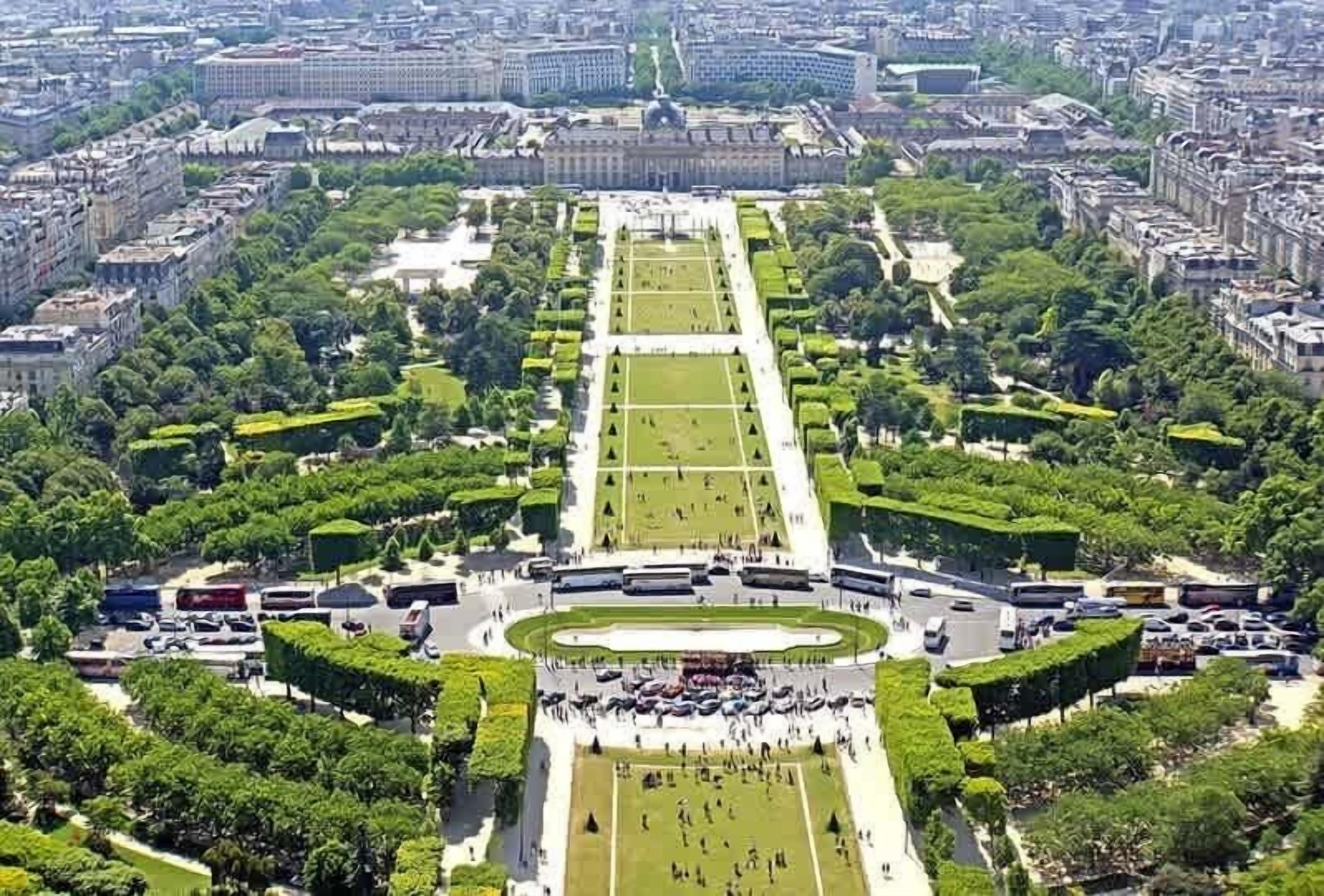An aerial view of a large, formal garden with symmetrical pathways and manicured lawns, surrounded by dense urban buildings.