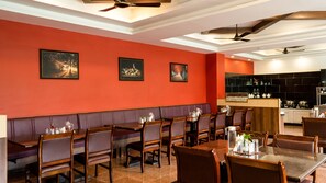 A restaurant with red walls, multiple dining tables, and ceiling fans. - Sakthi River Resorts (Anaimalai)