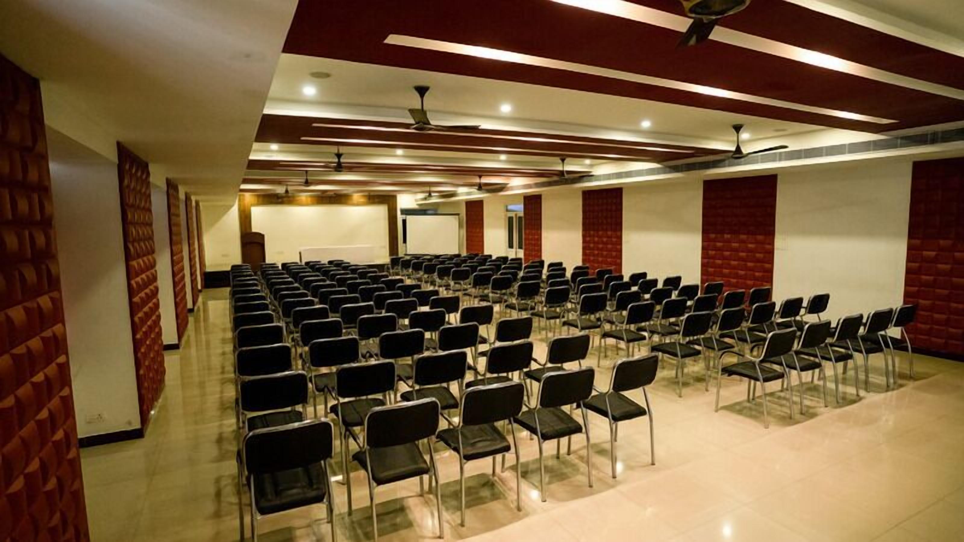 A conference room with rows of black chairs, a whiteboard, and a projector screen.