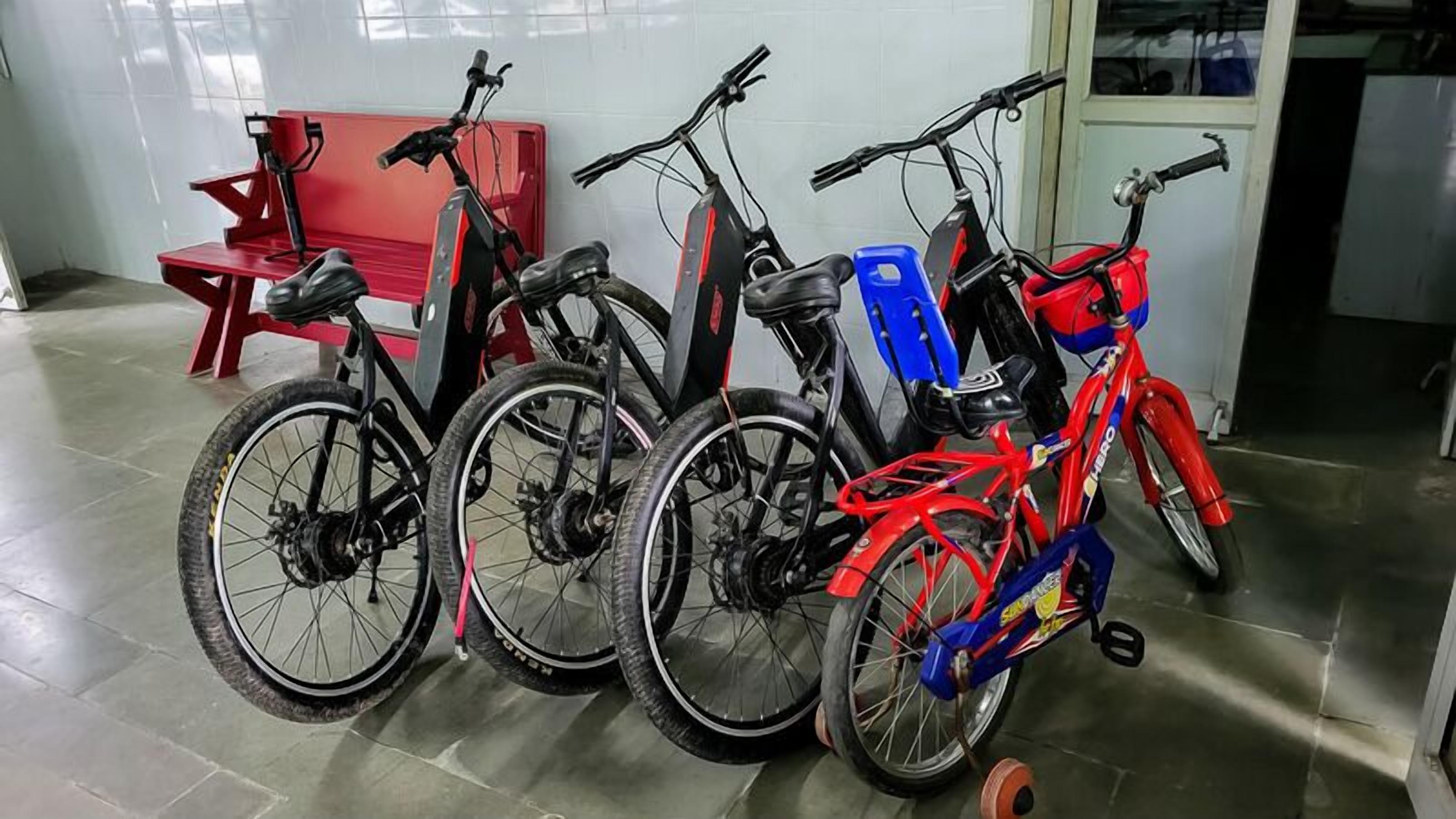 A row of bicycles parked indoors, with a red bench in the background.