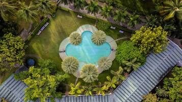 Vista aèria d'un complex turístic amb una piscina central envoltada de palmeres i una zona delimitada per una tanca.