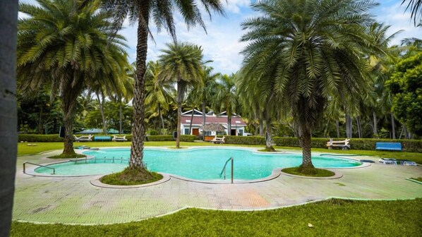 A swimming pool surrounded by palm trees and a building in the background. - Sakthi River Resorts (Anaimalai)