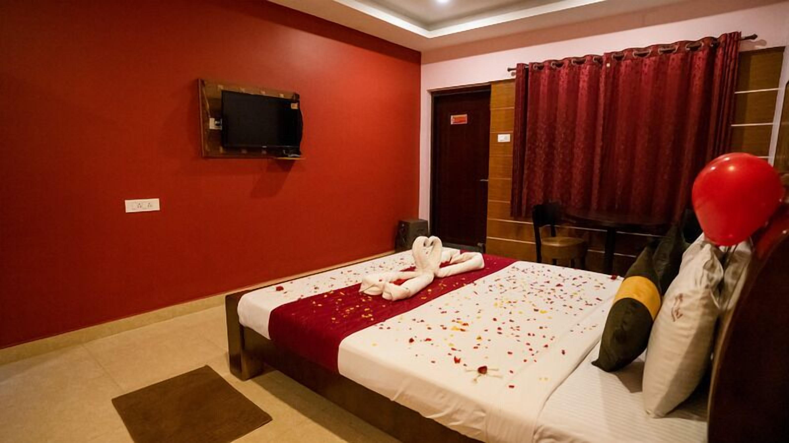 Ein Hotelzimmer mit roter Wand, einem Bett mit roter Bettdecke, einem an der Wand montierten Fernseher und einem roten Vorhang.