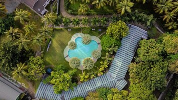 Vista aérea de un resort con una piscina central rodeada de palmeras y un paseo techado.