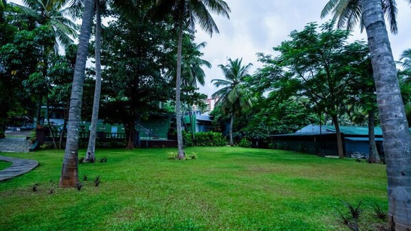 A lush green lawn with palm trees and a building in the background. - Sakthi River Resorts (Anaimalai)