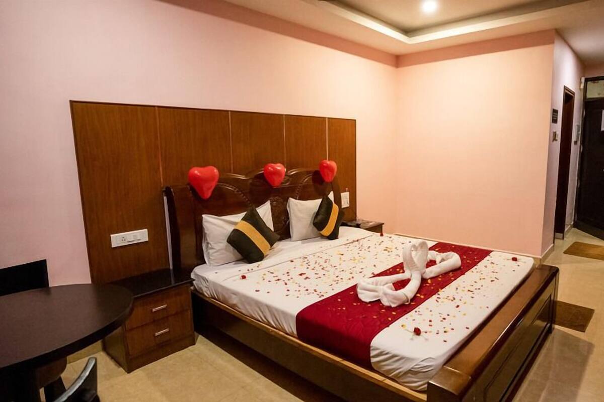 A hotel room with a wooden headboard, a bed with a red and white bedspread, and a heart-shaped decoration on the headboard.